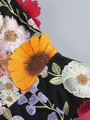 Close-up of a black fabric with colorful embroidered flowers on a gray background
