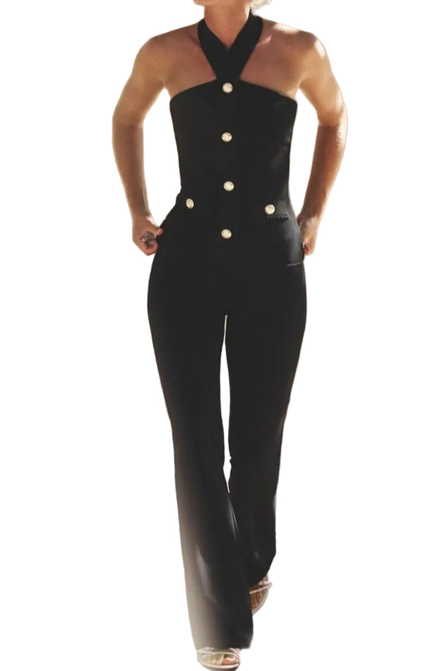 Person wearing a black jumpsuit with white buttons in a softly lit room.