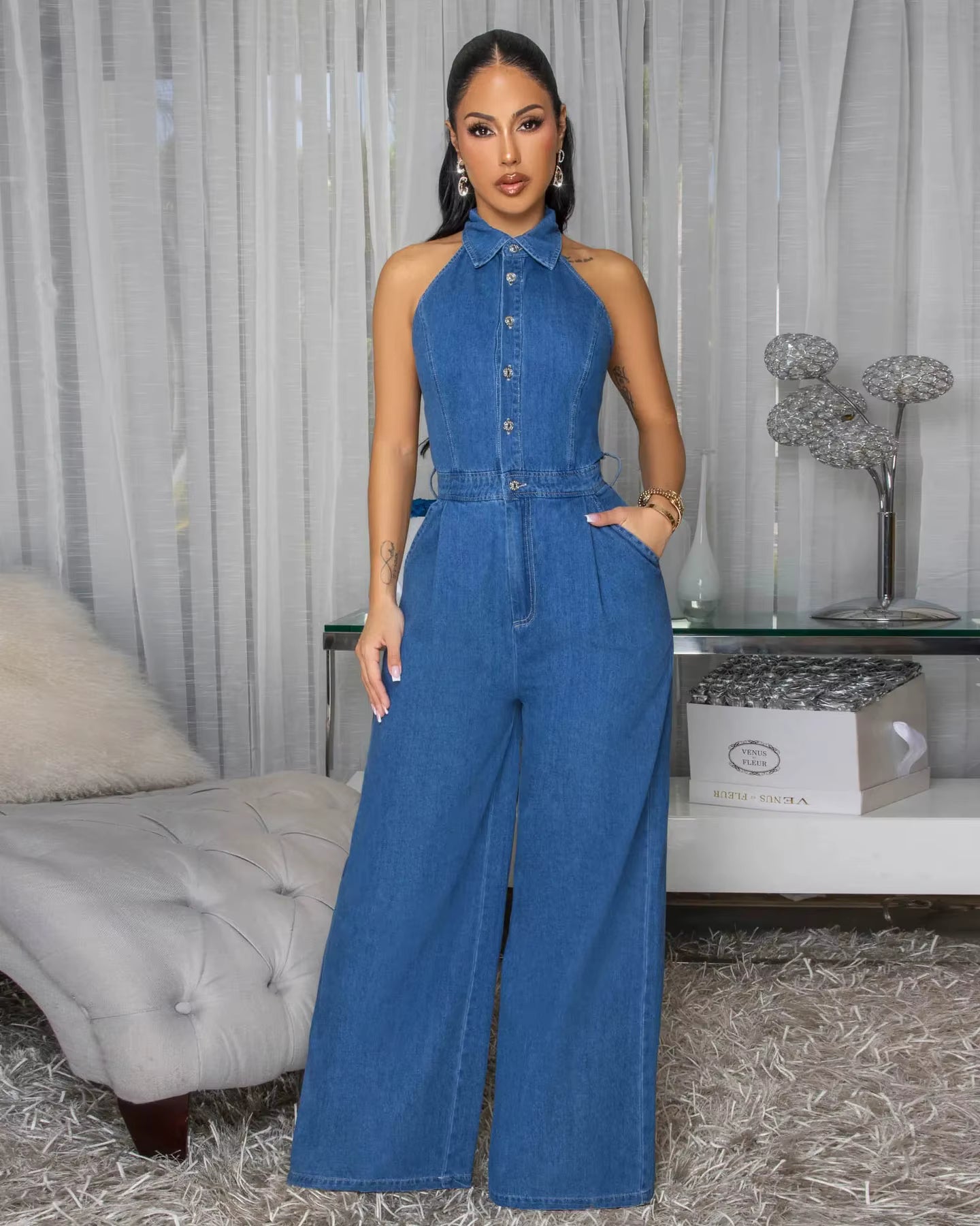 Woman wearing a blue denim jumpsuit in a room with a bed and decorative items.