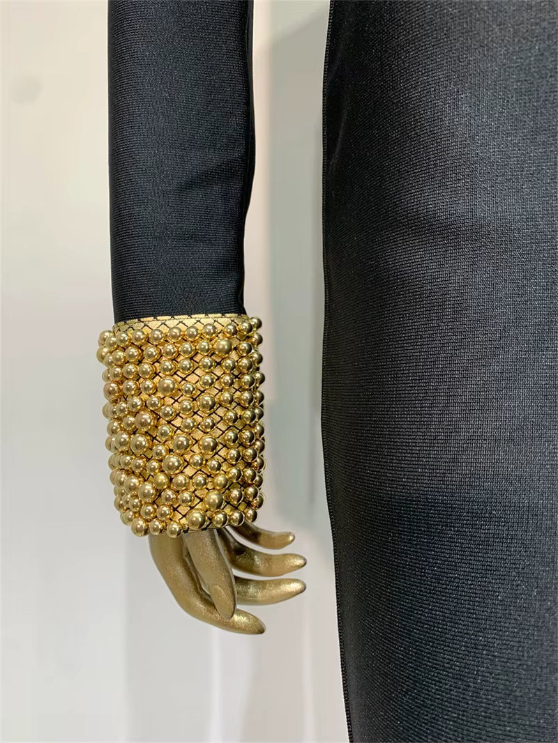 Gold beaded cuff on a black sleeve against a white background