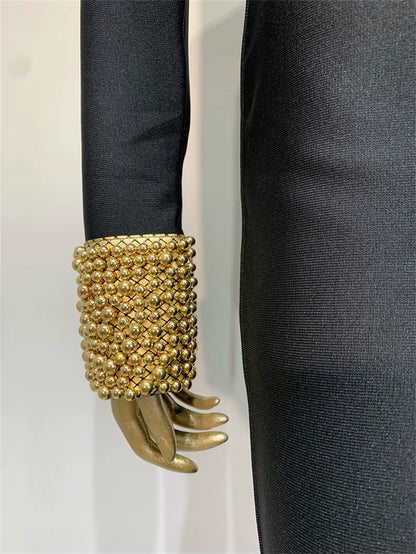 Gold beaded cuff on a black sleeve against a white background