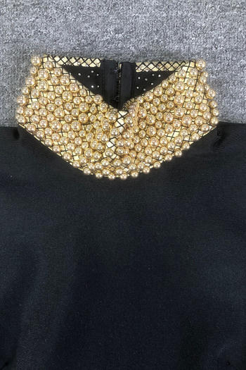 Black garment with a gold beaded collar on a textured gray background