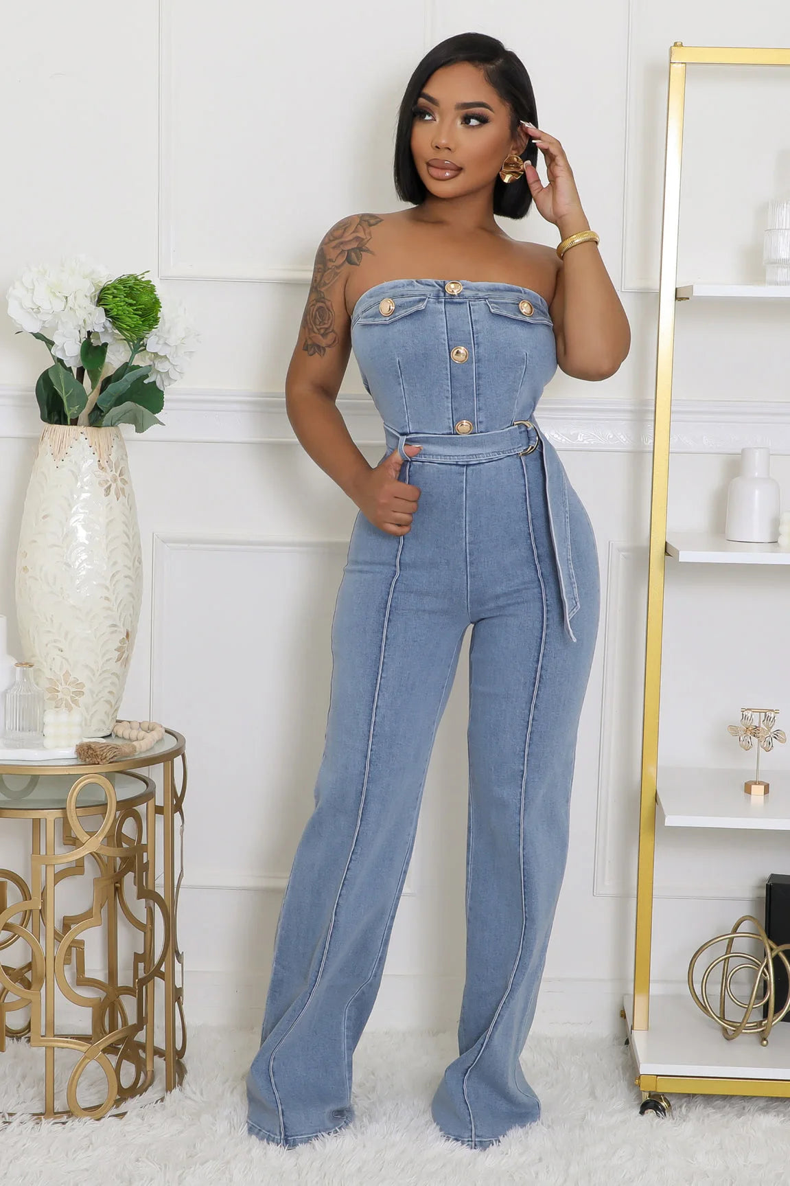 Woman wearing a denim jumpsuit standing in a stylish room with decor elements.